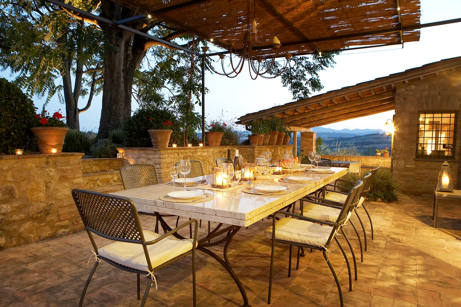 Long dining table laid for dinner under a shaded pergola